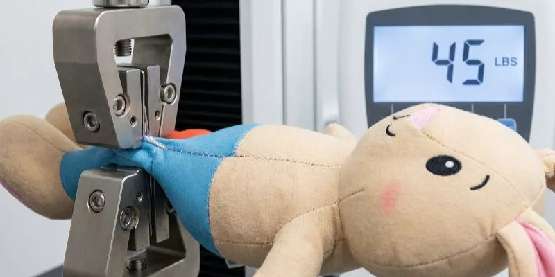 Tensile strength testing machine pulling a licensed character plush seam at 45 lbs
