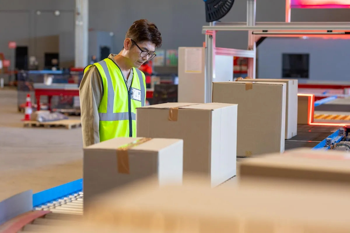 Worker in a hi-vis vest scanning plain cartons along a conveyor line