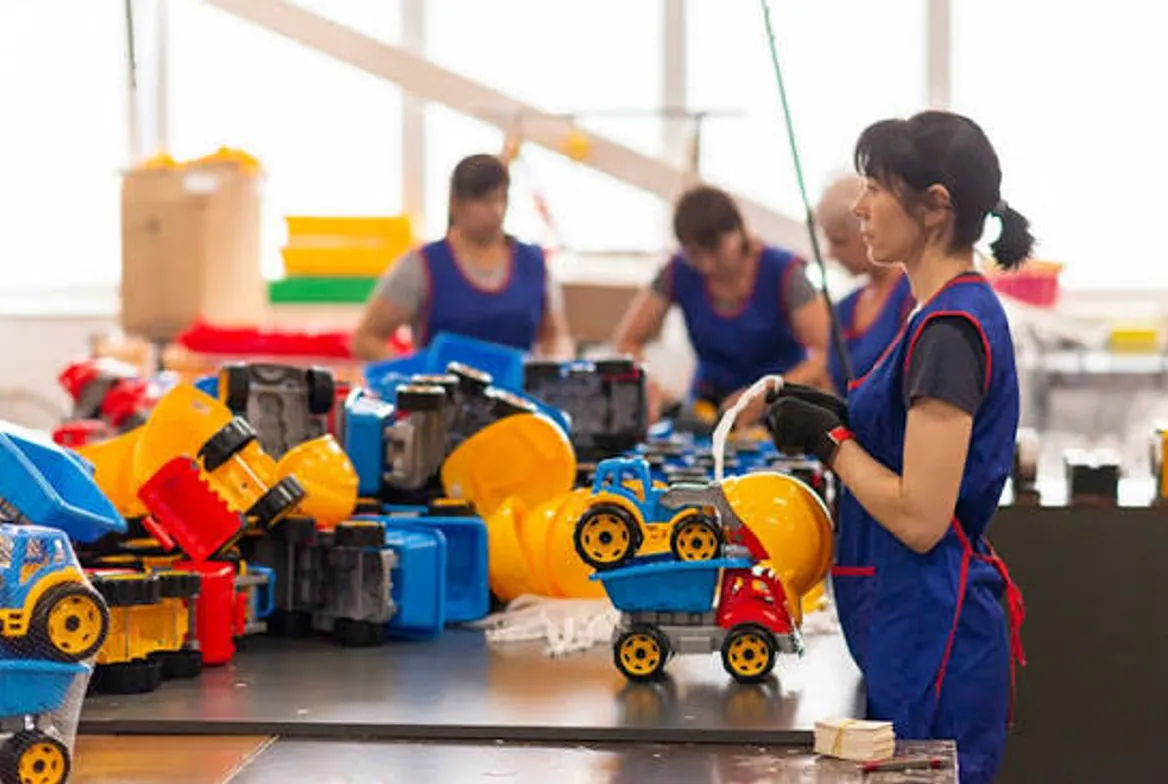 Workers assembling blue and yellow plastic toy trucks along a production bench