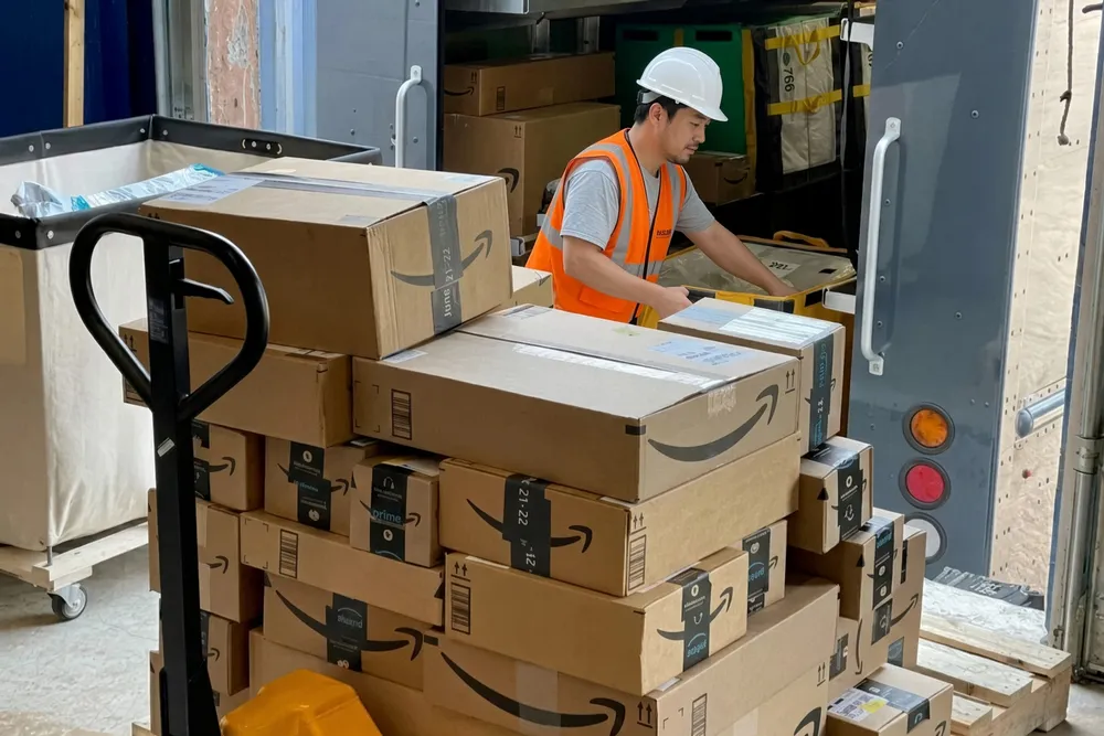 A pallet jack loaded with Amazon cartons being moved across a warehouse floor