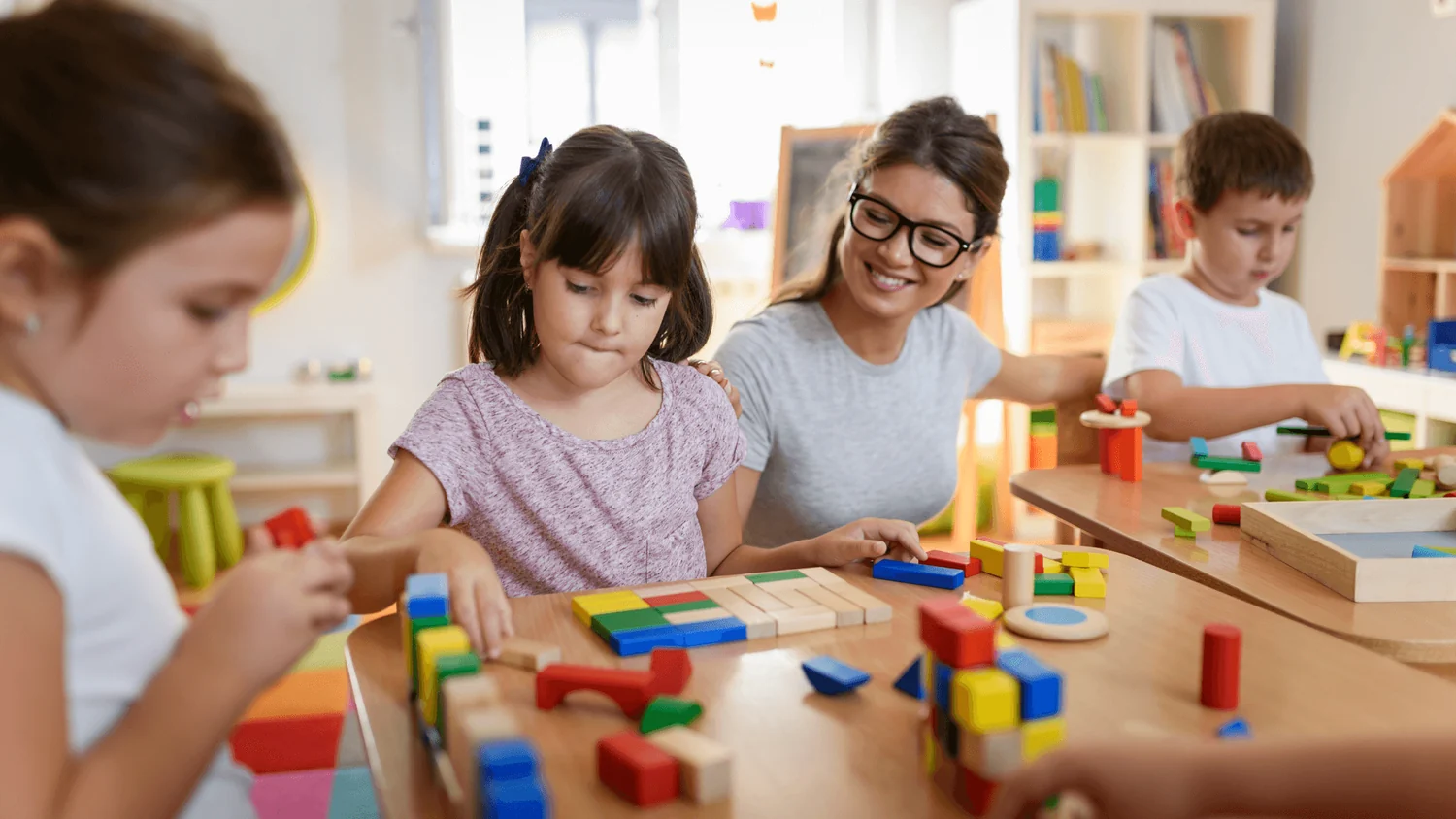 Natural wood Montessori materials including sensorial blocks, counting beads, and practical life tools in a prepared classroom environment